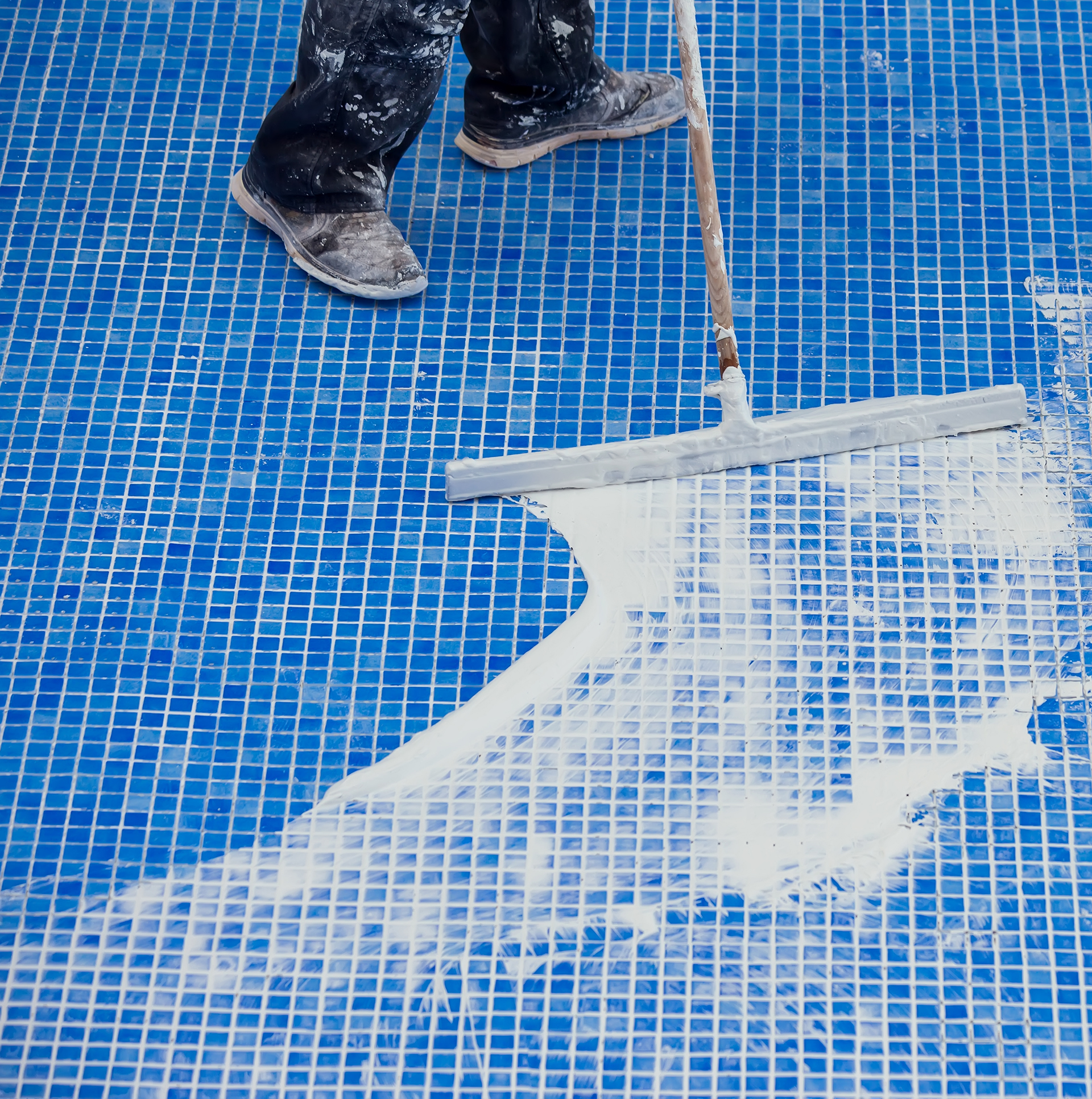 Worker covering seames on the tile in the pool. Pool repairing work